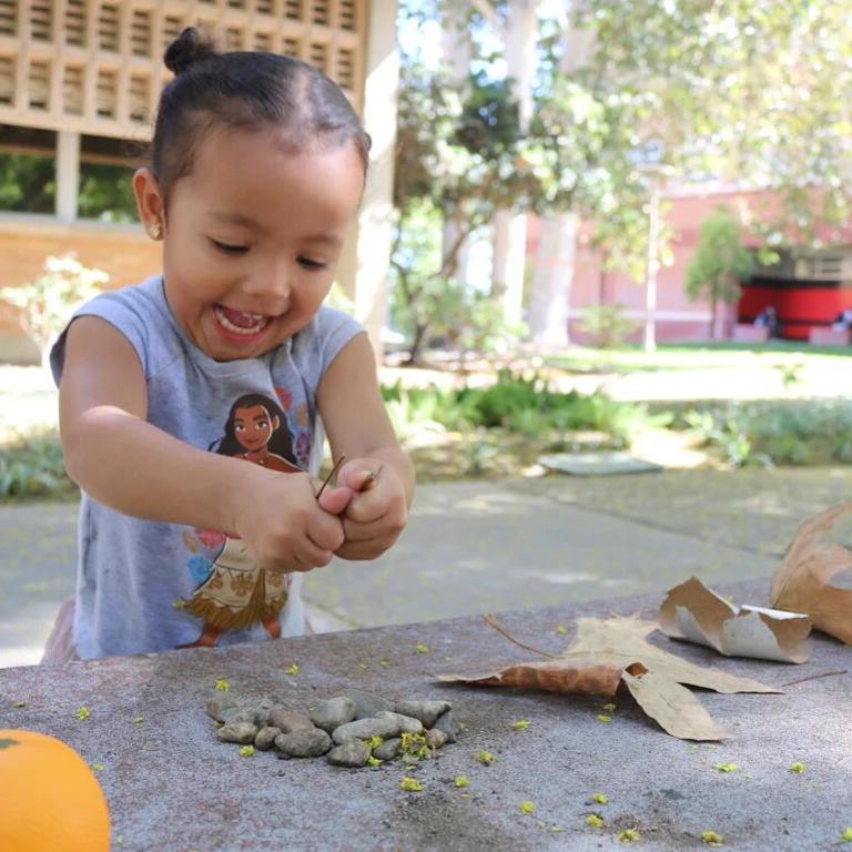 Small child at 博彩平台推荐 campus playing with leaves and rocks